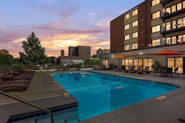 pool at dusk with a patio area and a community pool