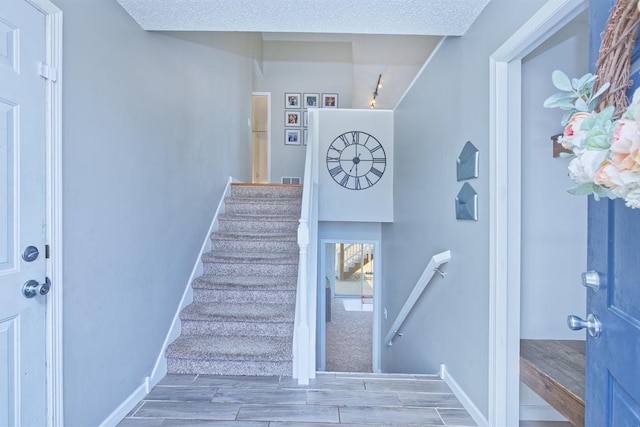 stairs featuring wood tiled floor, baseboards, and a textured ceiling