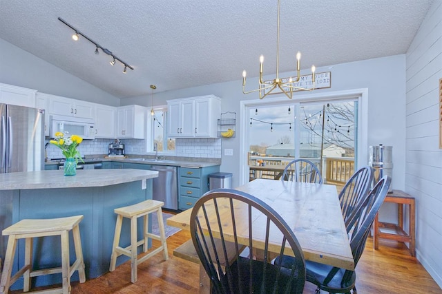 kitchen with white cabinets, lofted ceiling, appliances with stainless steel finishes, a kitchen breakfast bar, and wood finished floors