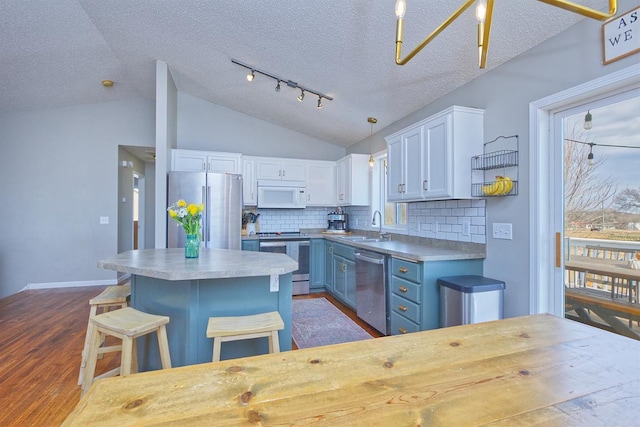 kitchen featuring stainless steel appliances, a sink, white cabinets, vaulted ceiling, and blue cabinetry