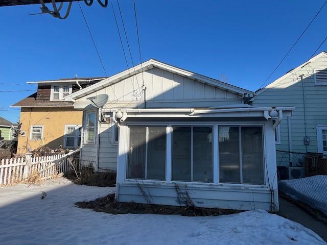 snow covered house featuring board and batten siding and fence