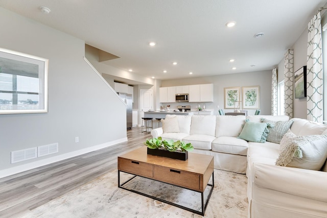 living room featuring light wood-style floors, baseboards, visible vents, and recessed lighting