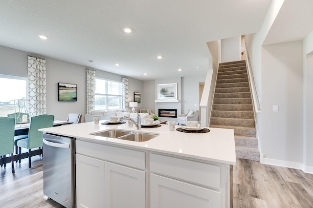 kitchen featuring a sink, white cabinets, open floor plan, stainless steel dishwasher, and a glass covered fireplace