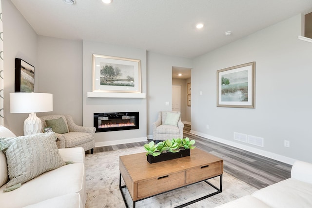 living room featuring recessed lighting, visible vents, baseboards, light wood-type flooring, and a glass covered fireplace