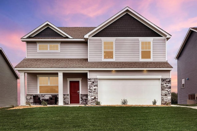 craftsman house with an attached garage, stone siding, a lawn, and roof with shingles