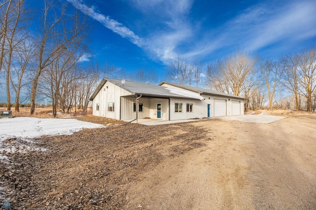 rear view of house featuring a garage, covered porch, dirt driveway, and board and batten siding