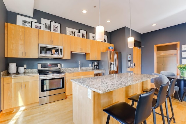 kitchen with a kitchen island, a kitchen bar, light stone counters, light wood-style flooring, and appliances with stainless steel finishes