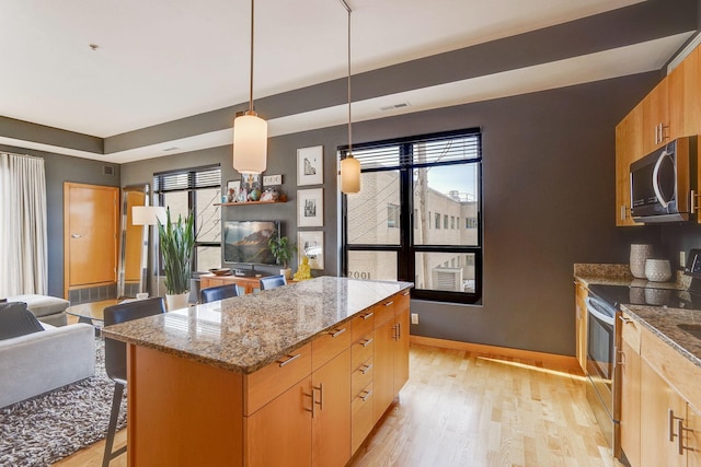 kitchen with a kitchen island, light stone countertops, open floor plan, light wood-style flooring, and appliances with stainless steel finishes