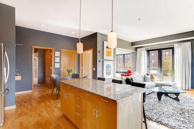 kitchen with a center island, light stone countertops, french doors, freestanding refrigerator, and light wood-style floors