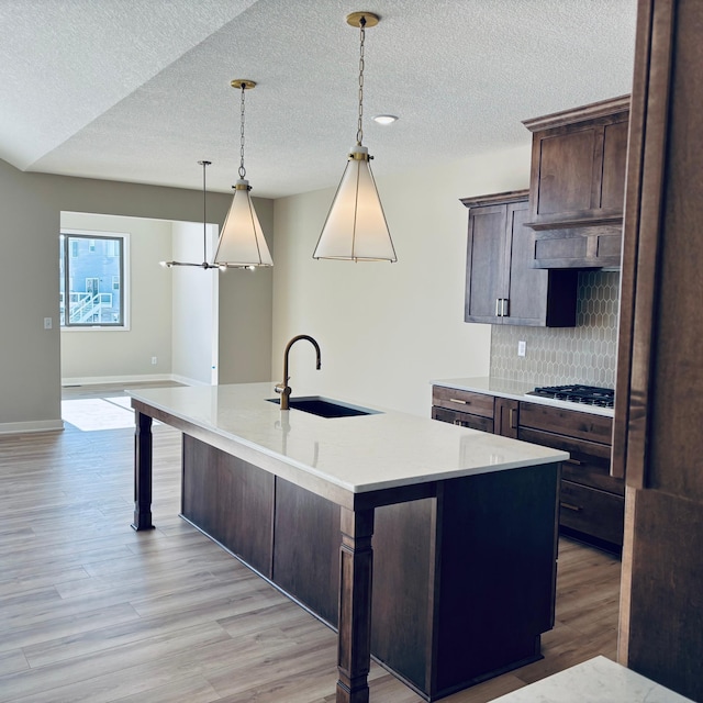 kitchen with a kitchen island with sink, a sink, light wood-style floors, light countertops, and tasteful backsplash