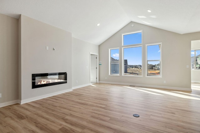 unfurnished living room featuring light wood finished floors, a glass covered fireplace, high vaulted ceiling, and baseboards