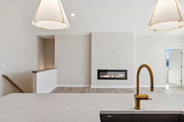 kitchen featuring wood finished floors, a sink, hanging light fixtures, light countertops, and a glass covered fireplace