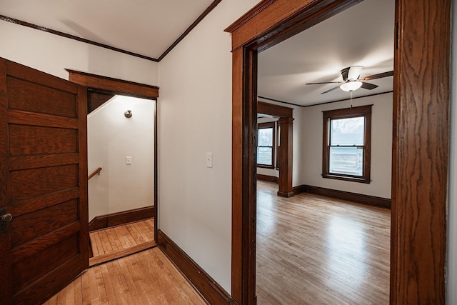 corridor with light wood-style floors, baseboards, and ornamental molding