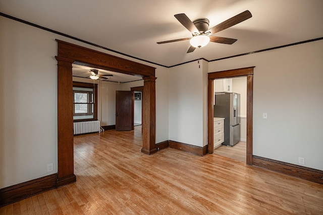 unfurnished room featuring radiator, ornate columns, light wood-style flooring, and ornamental molding