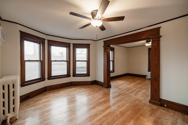 empty room with radiator heating unit, ornamental molding, light wood-style flooring, and baseboards