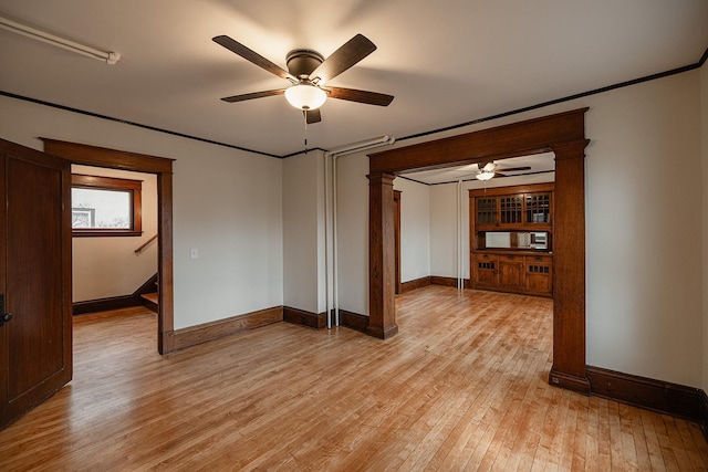 empty room featuring a ceiling fan, light wood-type flooring, decorative columns, and baseboards