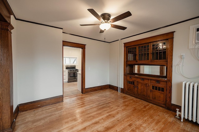 unfurnished room with ceiling fan, baseboards, light wood-type flooring, radiator heating unit, and crown molding