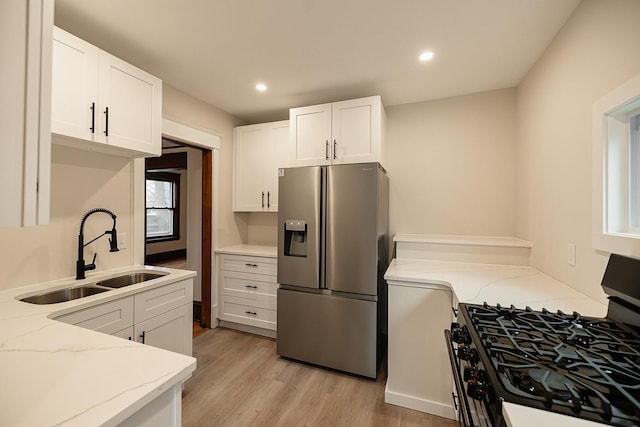 kitchen featuring light stone counters, stainless steel refrigerator with ice dispenser, gas range oven, light wood-style flooring, and a sink