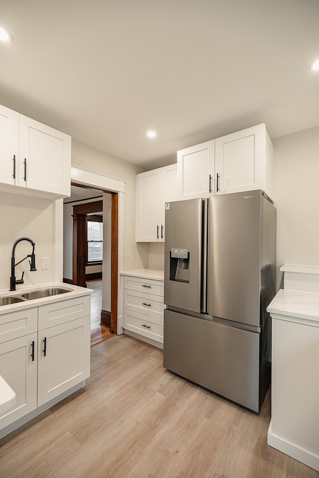 kitchen with white cabinets, stainless steel fridge, a sink, and light wood-style flooring