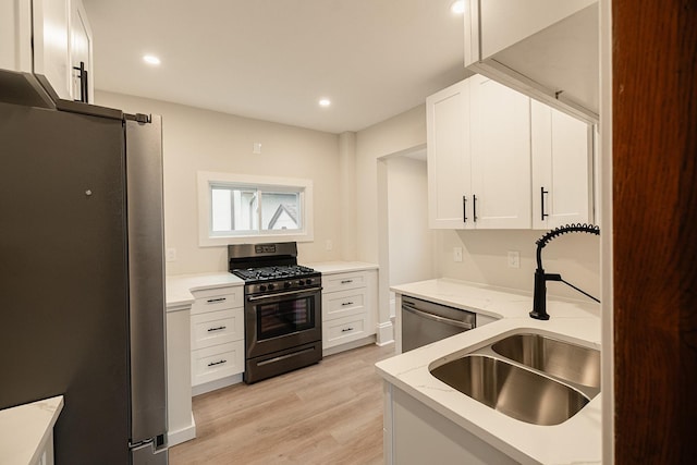 kitchen with light stone counters, light wood-style flooring, appliances with stainless steel finishes, white cabinetry, and a sink