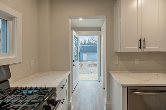 kitchen with light stone counters, white cabinets, stainless steel dishwasher, light wood-type flooring, and gas range oven