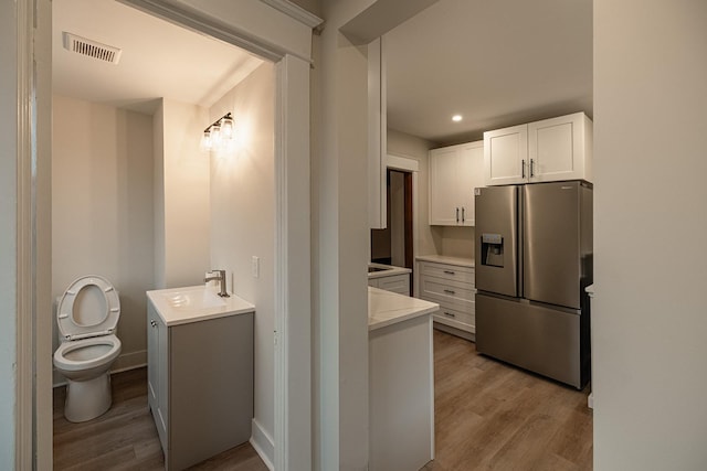 interior space with white cabinets, a sink, stainless steel refrigerator with ice dispenser, and wood finished floors