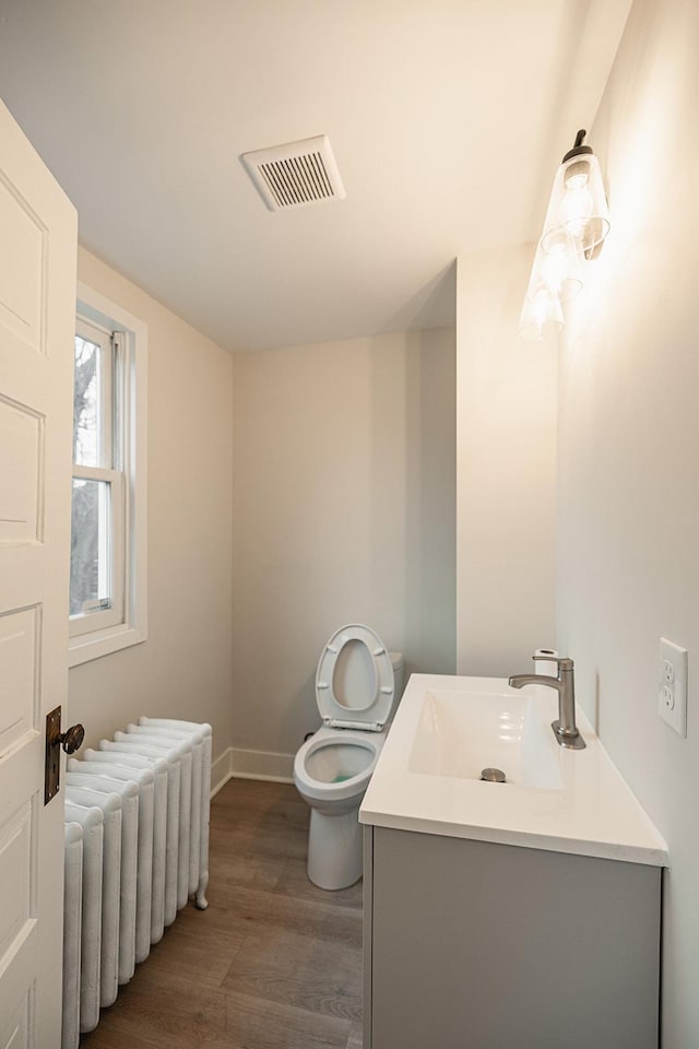 bathroom with visible vents, radiator, toilet, wood finished floors, and vanity