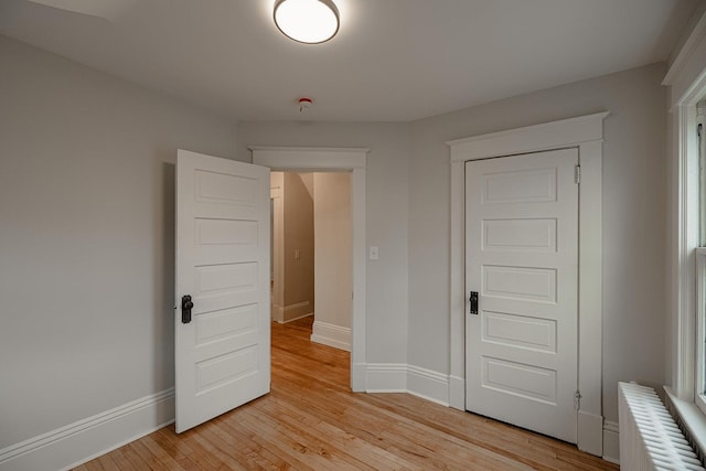 unfurnished bedroom featuring baseboards, light wood-style flooring, and radiator