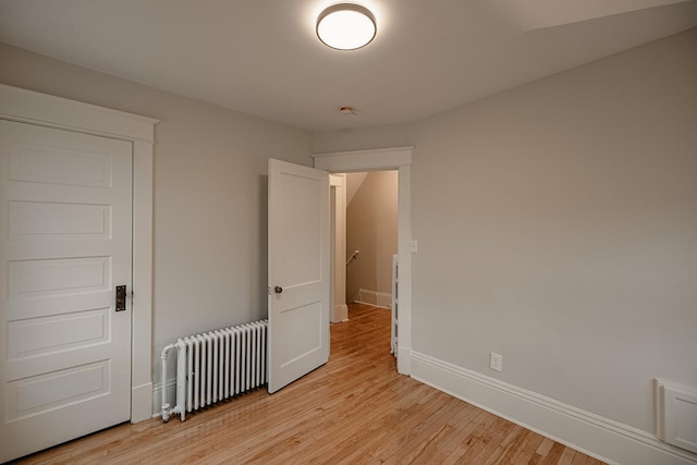 unfurnished bedroom with light wood finished floors, radiator heating unit, visible vents, and baseboards