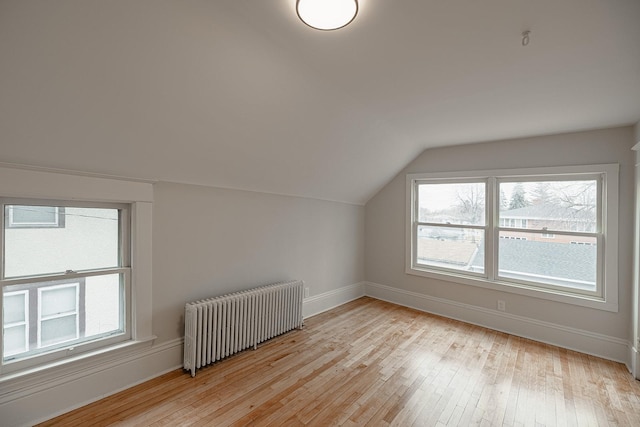 bonus room featuring vaulted ceiling, light wood finished floors, baseboards, and radiator