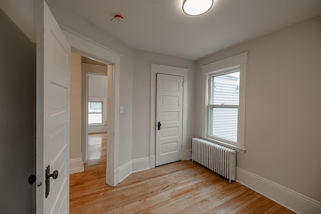 unfurnished bedroom with radiator, light wood-style floors, baseboards, and a closet