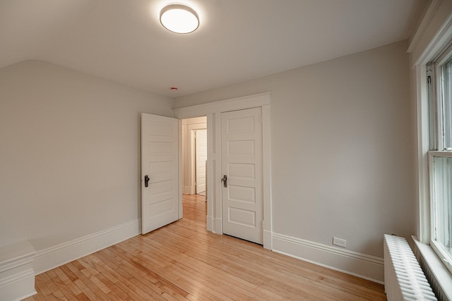 empty room featuring radiator, light wood-type flooring, and baseboards