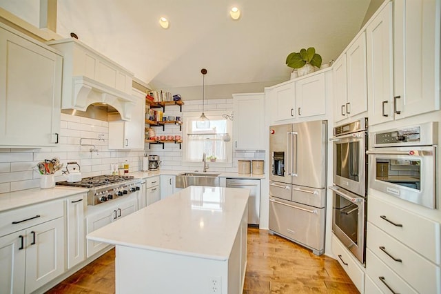 kitchen with stainless steel appliances, light countertops, decorative backsplash, vaulted ceiling, and a sink