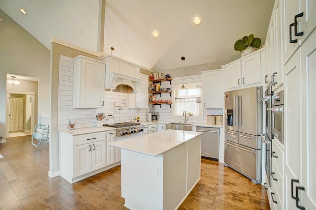 kitchen with a sink, vaulted ceiling, appliances with stainless steel finishes, custom exhaust hood, and light wood finished floors