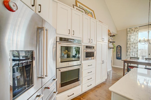 kitchen featuring a notable chandelier, hanging light fixtures, light wood-style flooring, appliances with stainless steel finishes, and vaulted ceiling