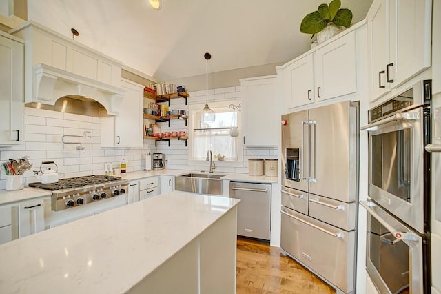 kitchen with a sink, white cabinets, vaulted ceiling, appliances with stainless steel finishes, and tasteful backsplash