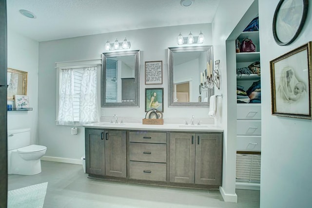 bathroom with baseboards, a sink, toilet, and double vanity