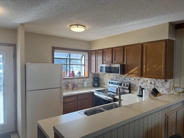 kitchen with tasteful backsplash, light countertops, a peninsula, stainless steel appliances, and a sink