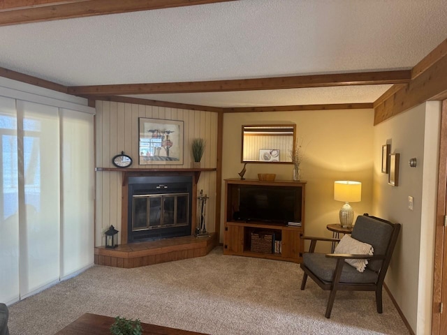 living room featuring a glass covered fireplace, beamed ceiling, carpet floors, and a textured ceiling