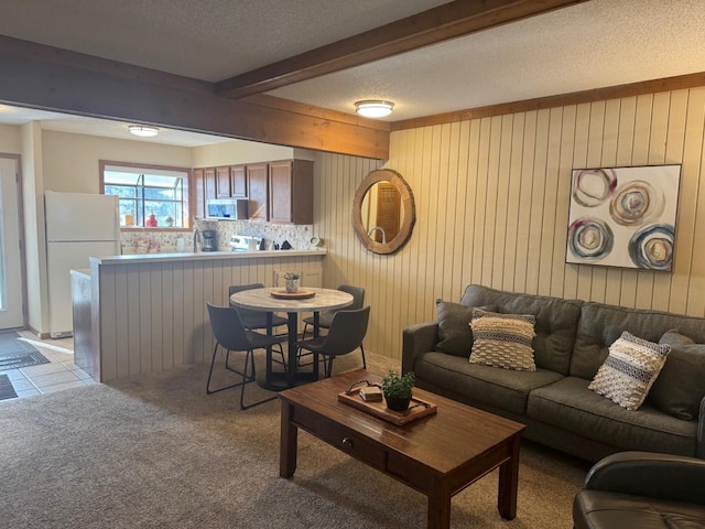 living area featuring beamed ceiling, light carpet, a textured ceiling, wood walls, and light tile patterned floors