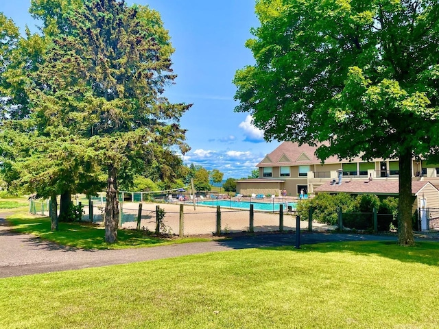 view of property's community featuring a swimming pool, a lawn, and fence