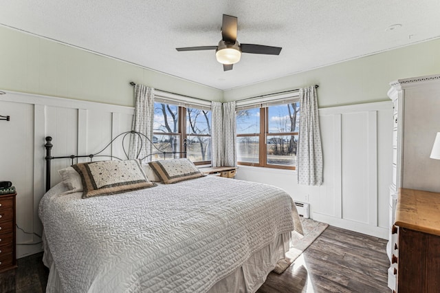 bedroom with a textured ceiling, a baseboard heating unit, a decorative wall, and dark wood-style flooring