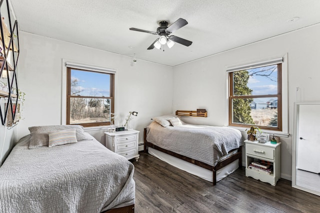 bedroom with dark wood-style floors, multiple windows, a baseboard heating unit, and a textured ceiling