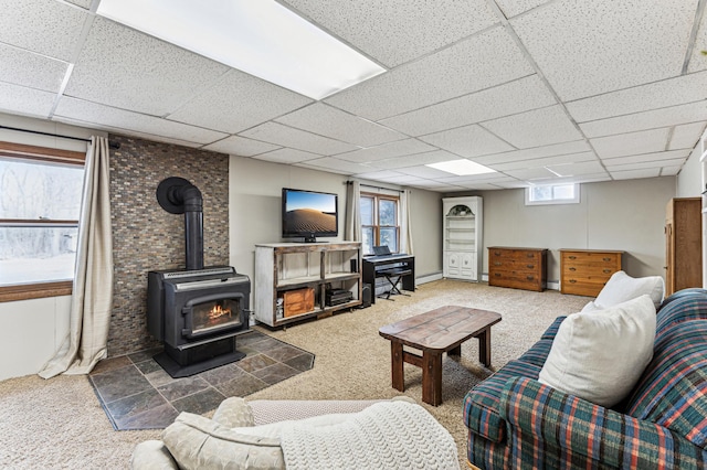 carpeted living area with a paneled ceiling, a baseboard radiator, and a wood stove