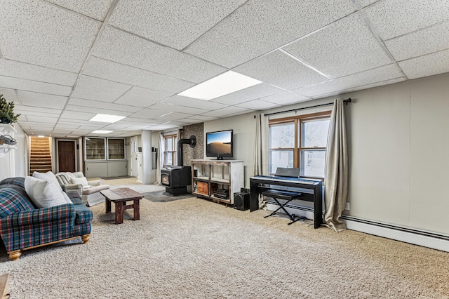 carpeted living room with a baseboard heating unit, a paneled ceiling, and a wood stove