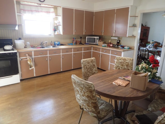 kitchen featuring a sink, light countertops, light wood-type flooring, stainless steel microwave, and range with gas cooktop