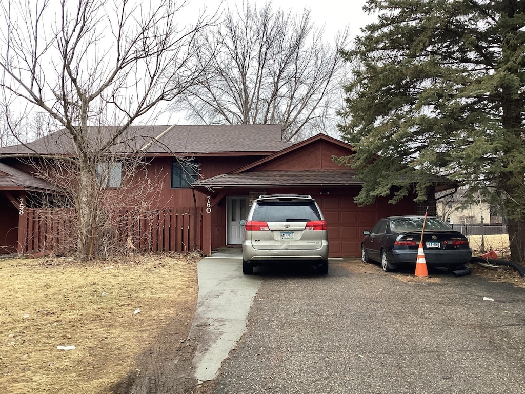 view of side of property featuring aphalt driveway, an attached garage, roof with shingles, and fence