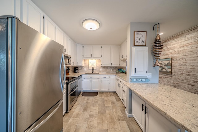 kitchen featuring light stone counters, stainless steel appliances, decorative backsplash, white cabinetry, and a sink