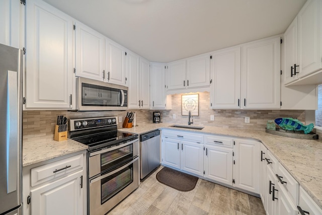 kitchen featuring decorative backsplash, appliances with stainless steel finishes, light stone countertops, white cabinetry, and a sink