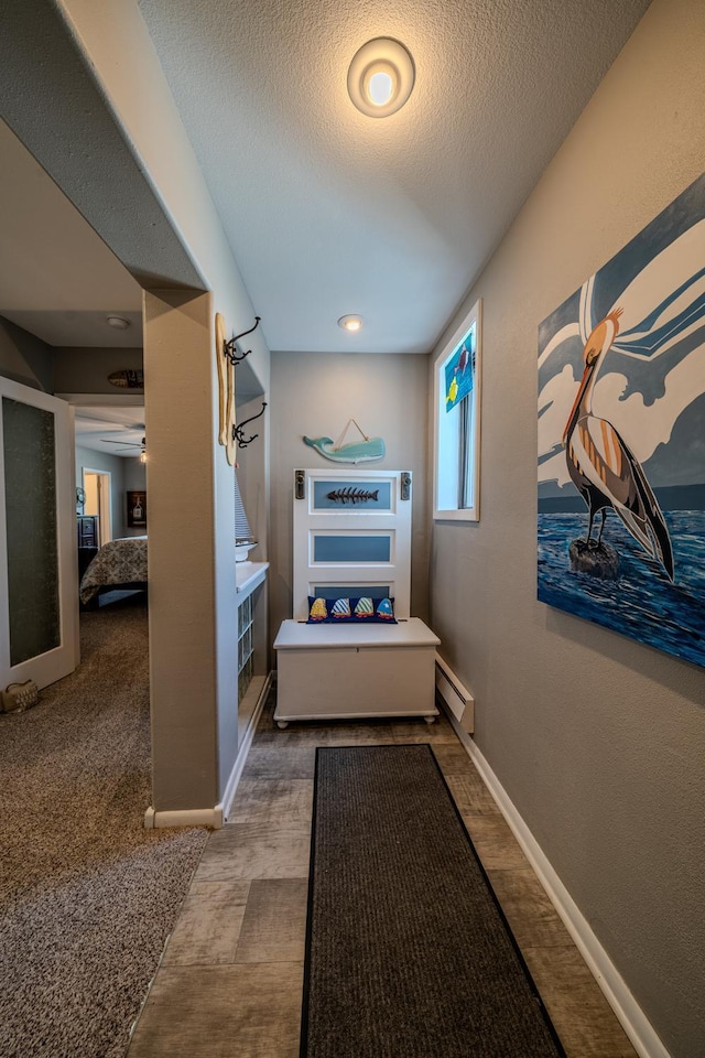 hallway featuring a baseboard radiator, baseboards, and a textured ceiling